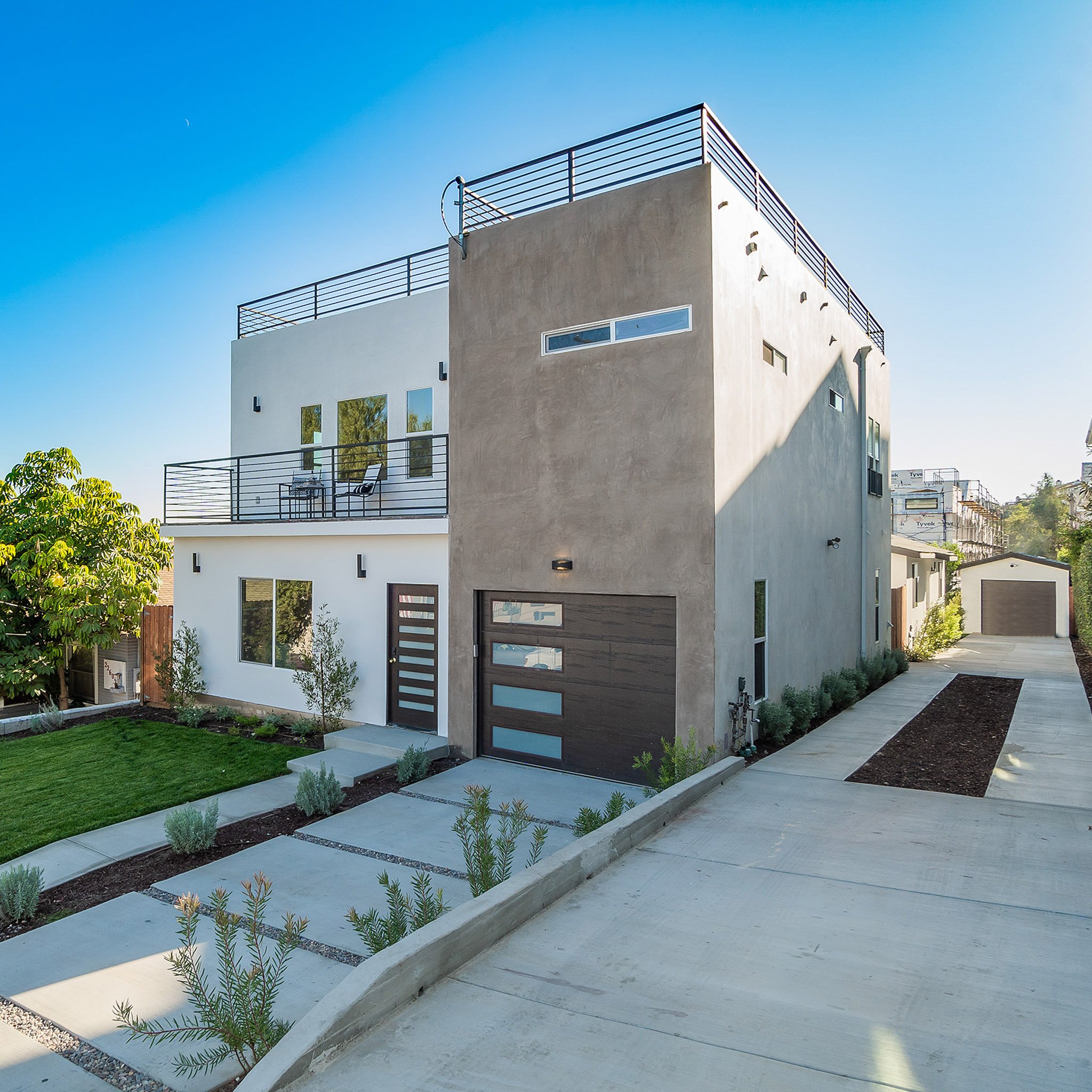 Modern three-story residential home with rooftop deck, stucco exterior, and private driveway in Los Angeles.