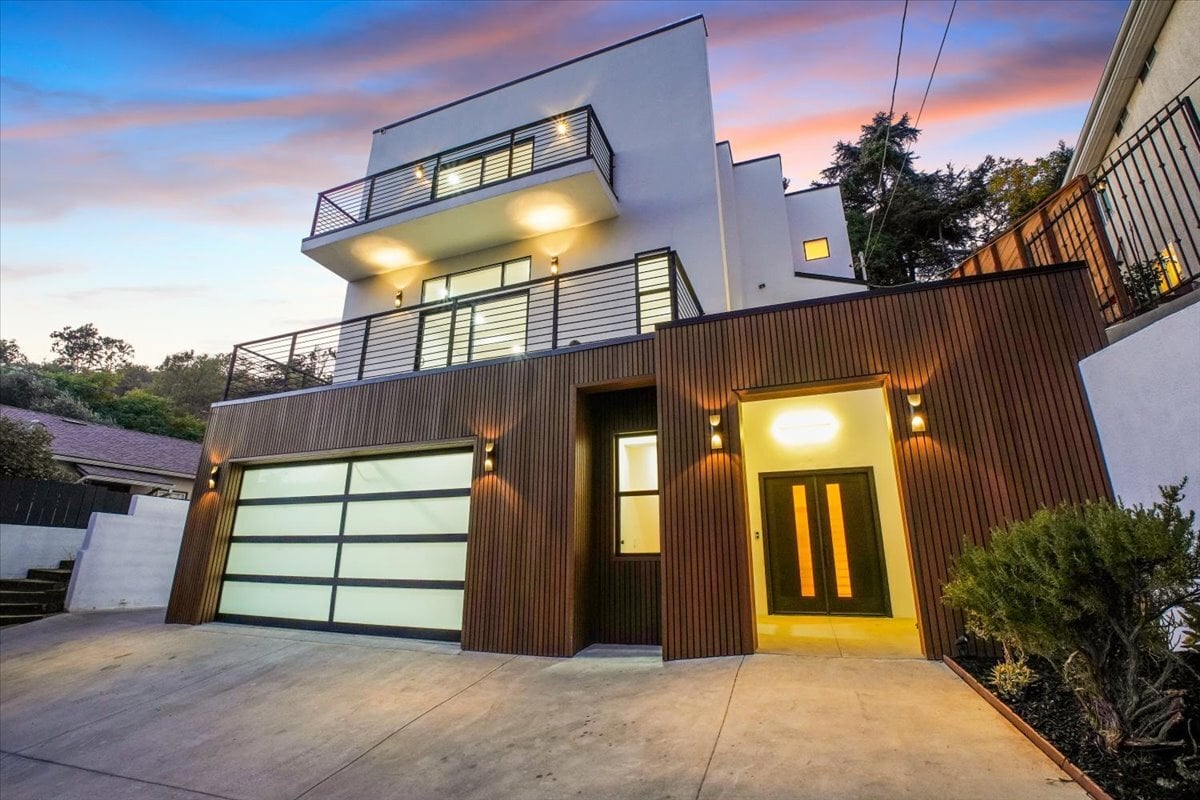 Modern multi-level hillside home with large glass windows and warm exterior lighting at dusk.