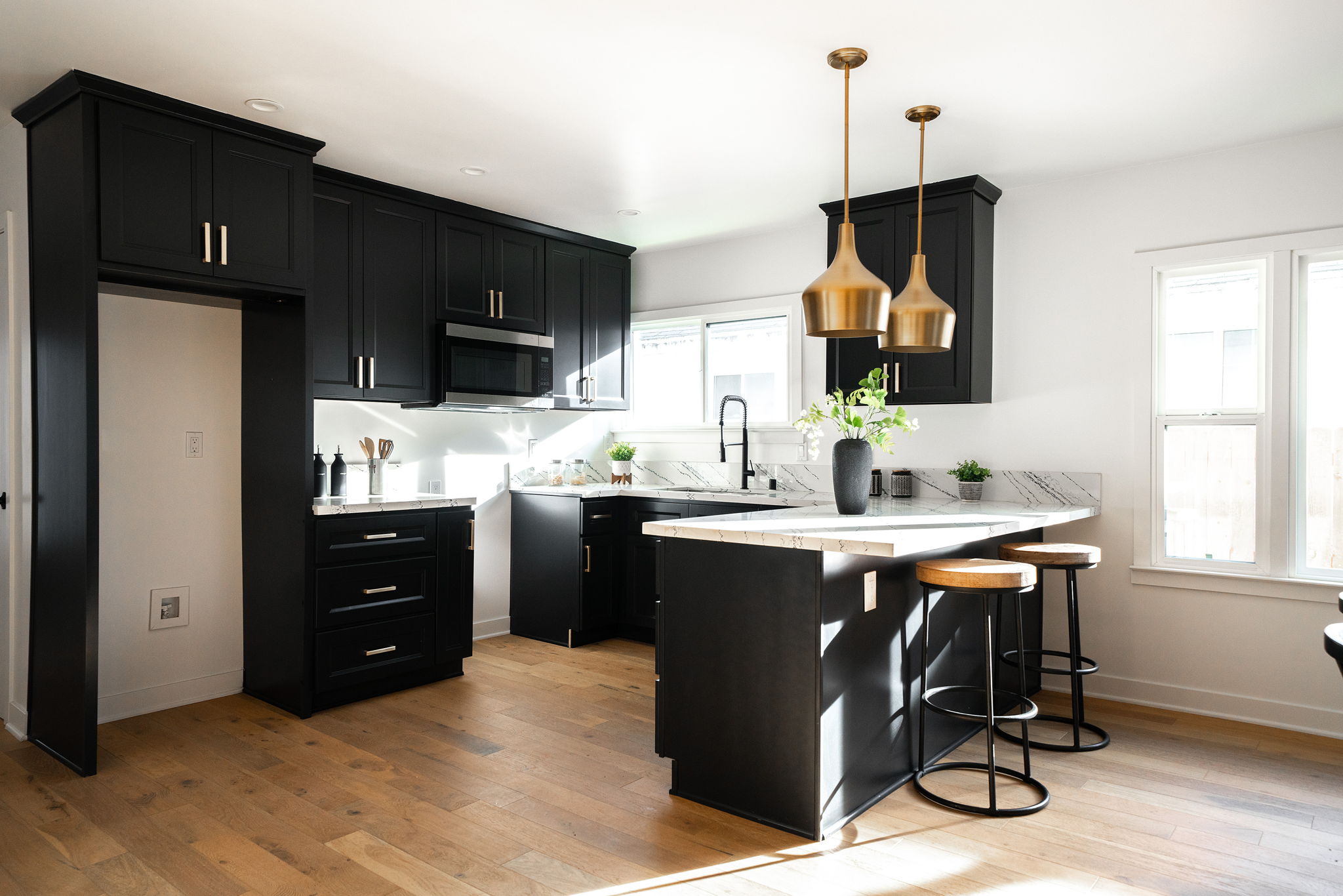 Modern kitchen with black cabinetry, white counters, and gold pendant lighting.