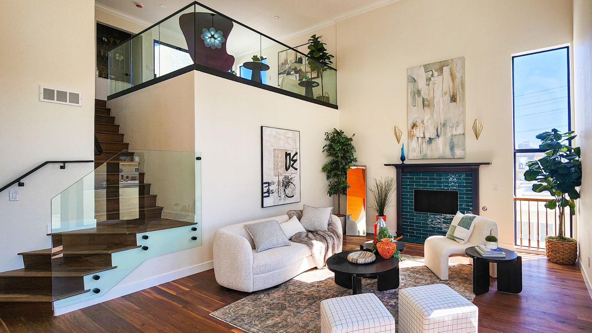 Modern residential living room with open loft layout, custom wood staircase with glass railing, hardwood flooring, and contemporary fireplace design.