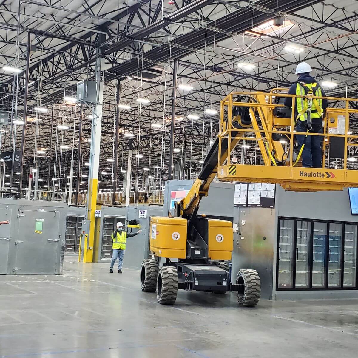 ATP Development & Construction crew operating a boom lift during active commercial warehouse build-out, with workers in safety gear on the job floor of a large industrial facility in Los Angeles