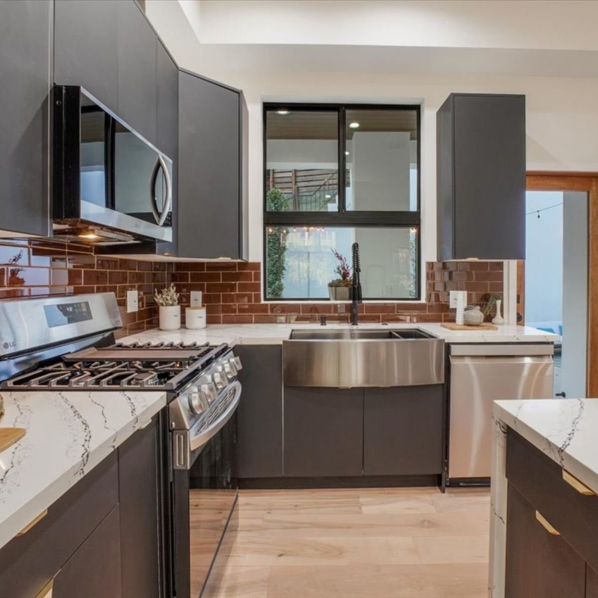 Completed modern kitchen interior by ATP Development & Construction featuring quartz countertops, dark cabinetry, terra cotta tile backsplash, farmhouse sink, and hardwood flooring in a Los Angeles residential project